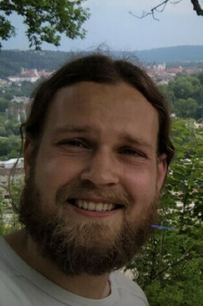 Fabian Jakubczyk lächelnd, draußen mit Landschaft im Hintergrund.